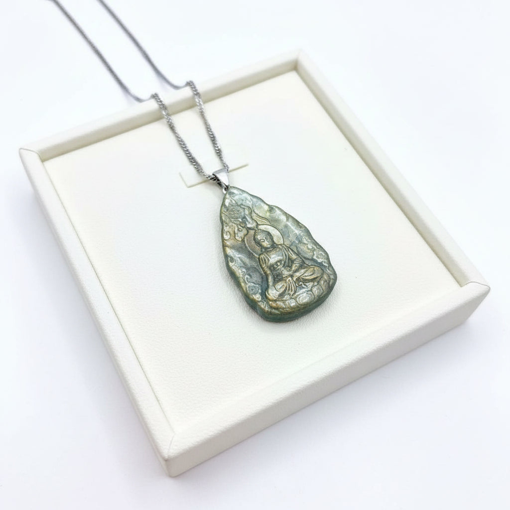 A silver-toned pendant necklace featuring an engraved Buddha figure on a textured, irregular stone pendant, resting on a rustic wood slice background.