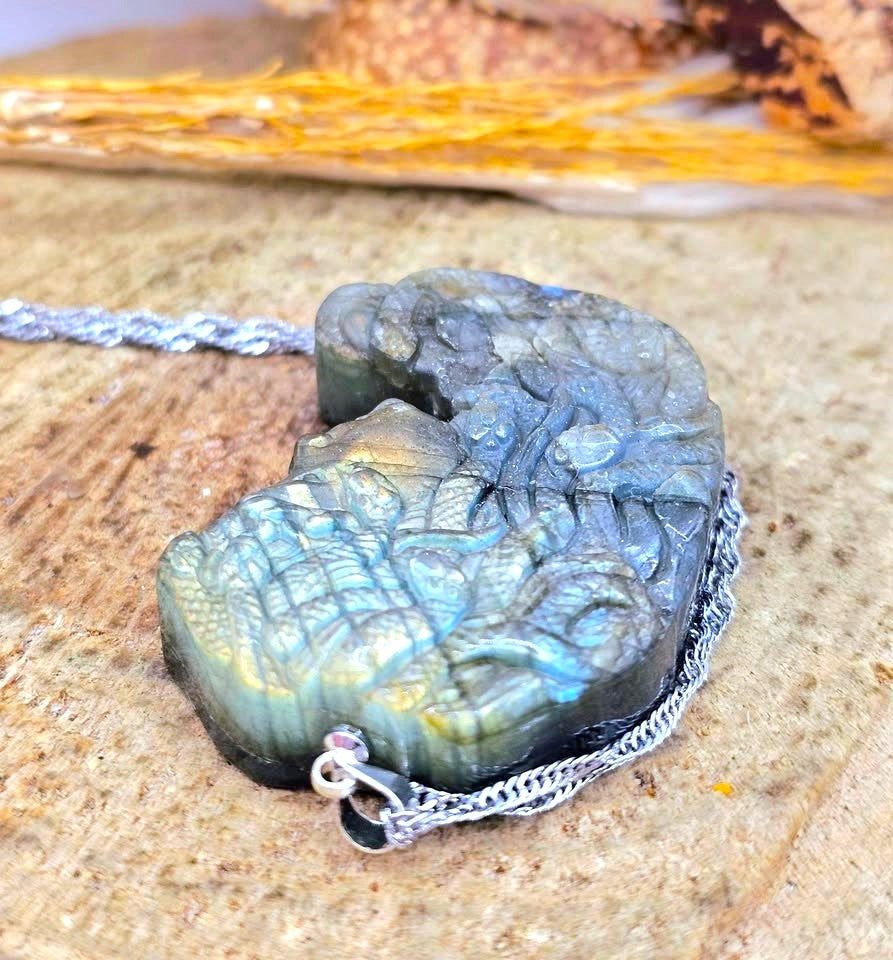 A carved labradorite pendant necklace with a silver-toned chain, resting on a textured stone surface.