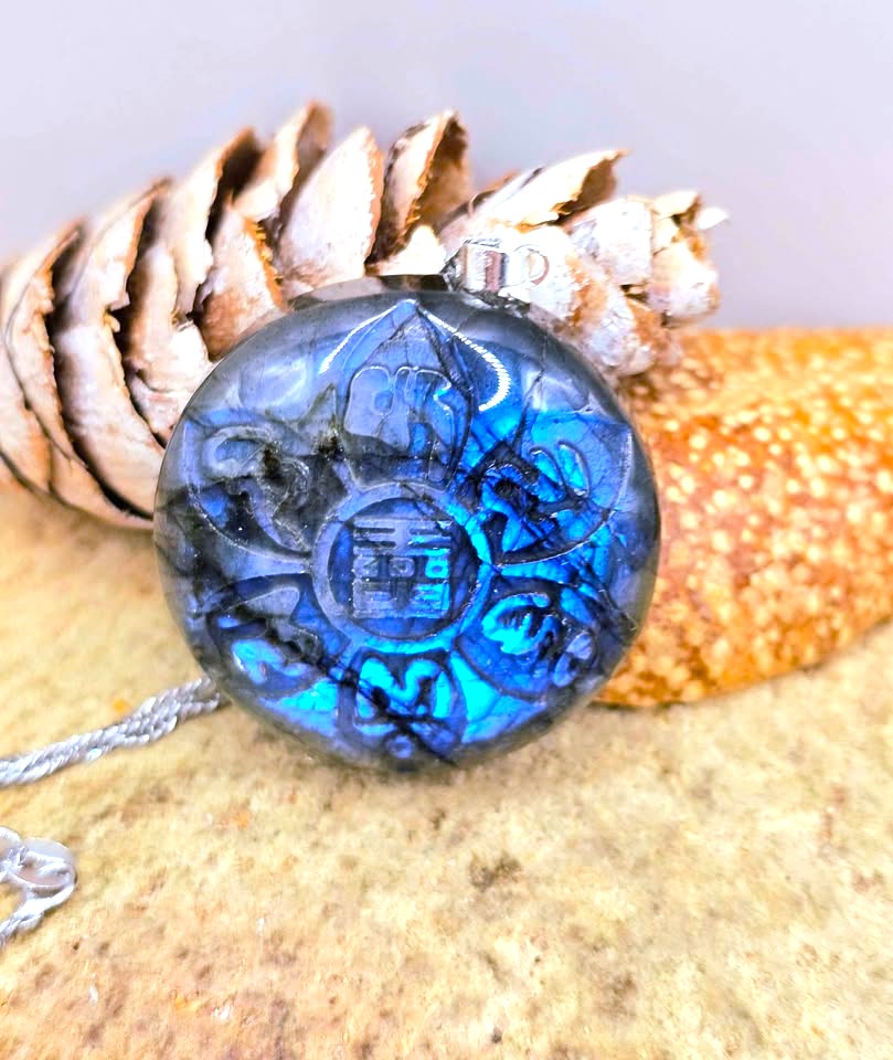 A round labradorite pendant lotus carving , resting on a pinecone and textured stone surface.