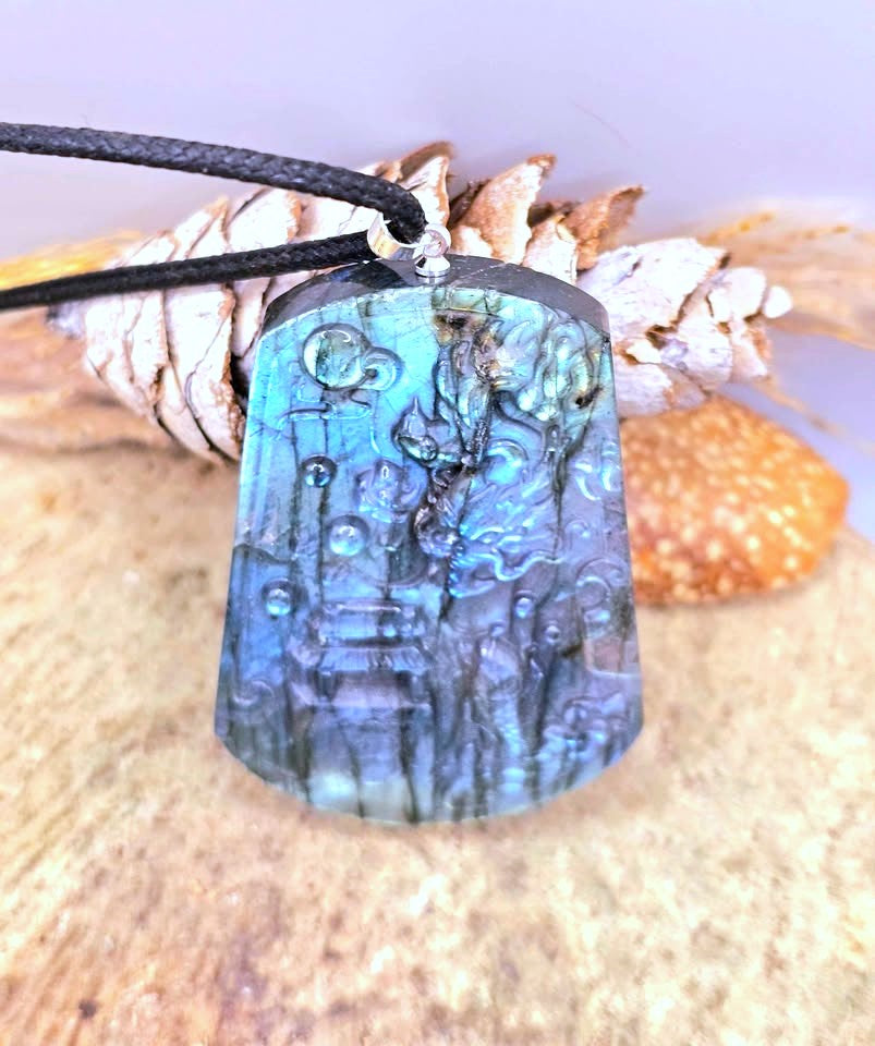 A carved labradorite pendant necklace with a black cord, resting on a pine cone and wood slice against a soft lavender background.