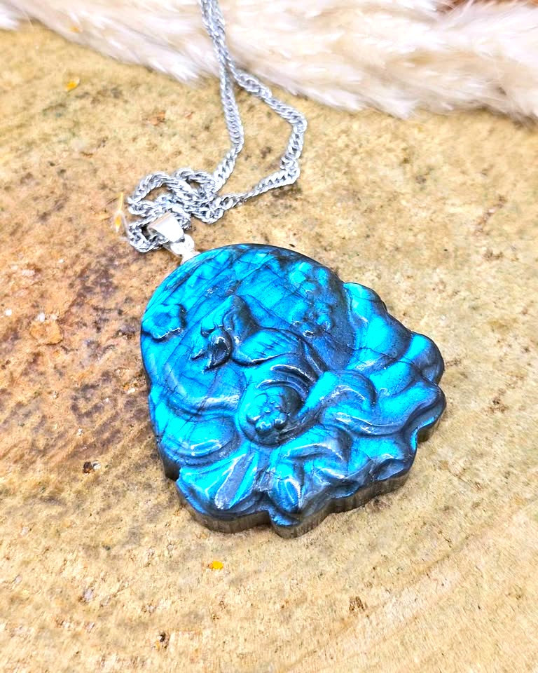 A carved turquoise and dark blue stone pendant necklace with a silver chain, displayed on a textured tan stone surface.