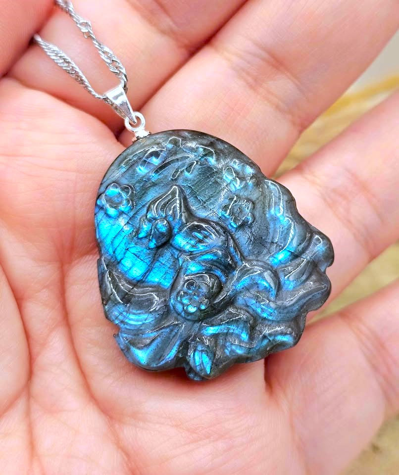 A close-up of a hand holding a silver chain necklace with a highly textured, organic-shaped labradorite pendant that glows with vibrant blue iridescence.