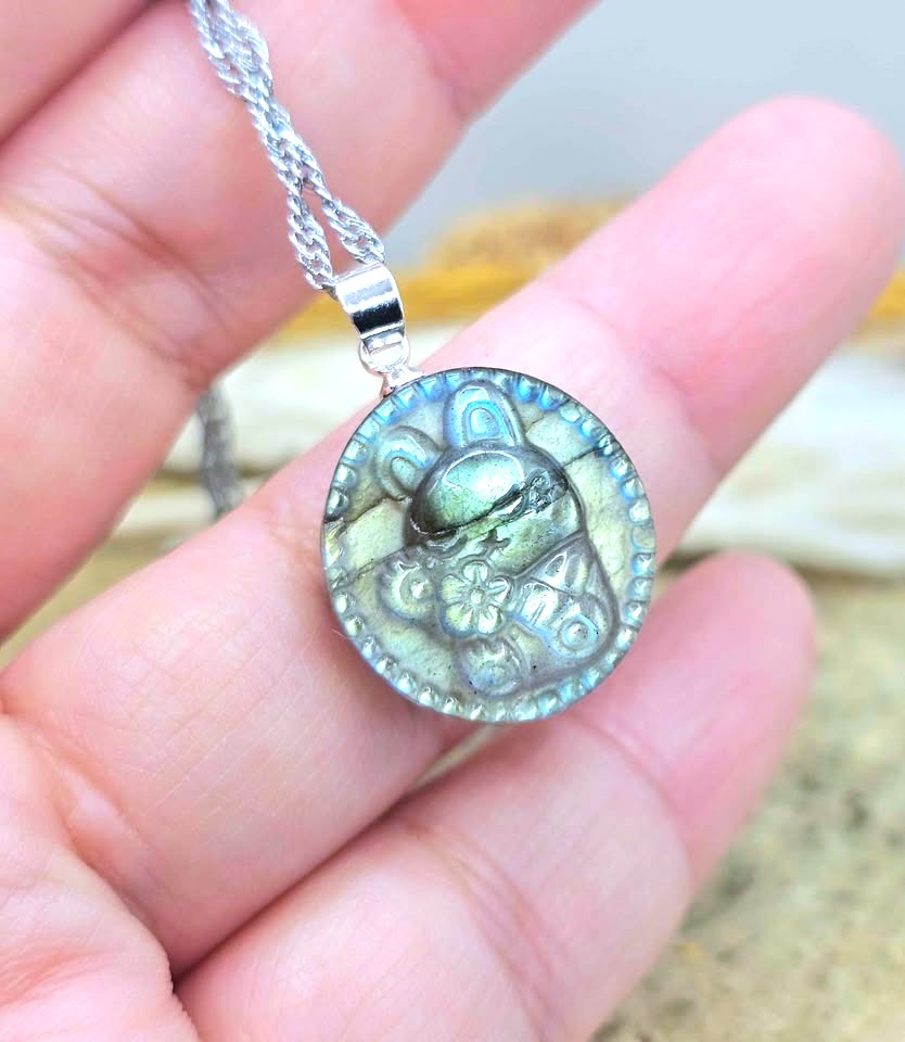 A silver pendant necklace featuring a circular, textured green stone with a carved bear design, held in a person's hand.