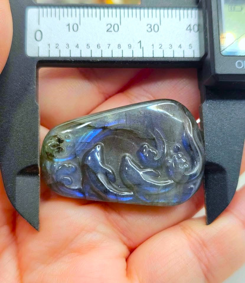 Carved labradorite dolphin pendant held in hand under a caliper to show its size — My Aura Gemstones