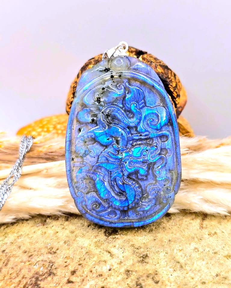 A carved blue stone pendant with a dragon motif, resting on a textured surface with a silver chain partially visible.
