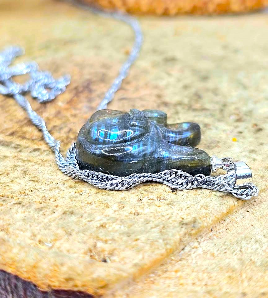 A silver-toned chain necklace with a polished dark green labradorite pendant resting on a textured tan stone surface.