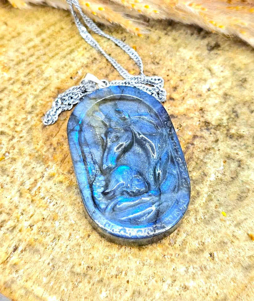 A carved oval pendant necklace featuring a blue marbled design with a silver-toned chain, displayed on a textured beige stone surface.