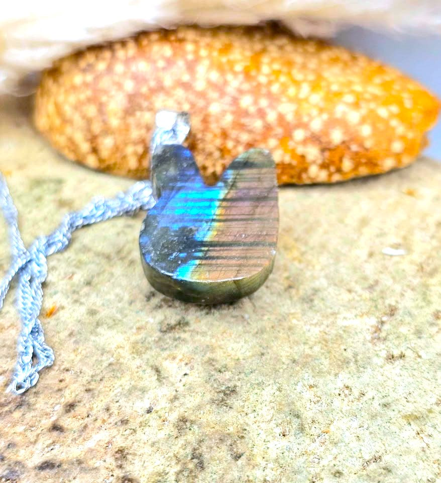 A polished labradorite pendant necklace with a silver bail, resting on a textured stone surface with a blurred starfish in the background.