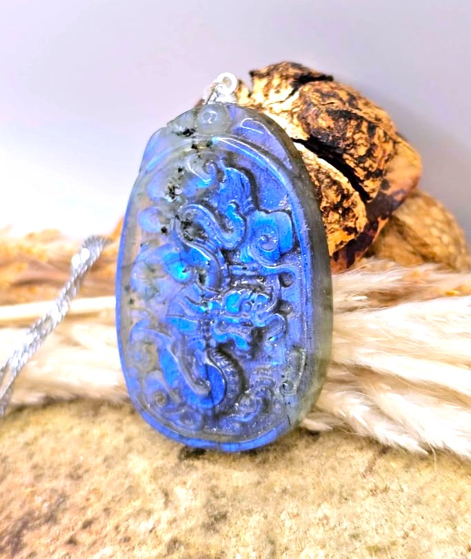 A carved blue pendant necklace with a dragon design, resting on a textured surface with fur and bark props.