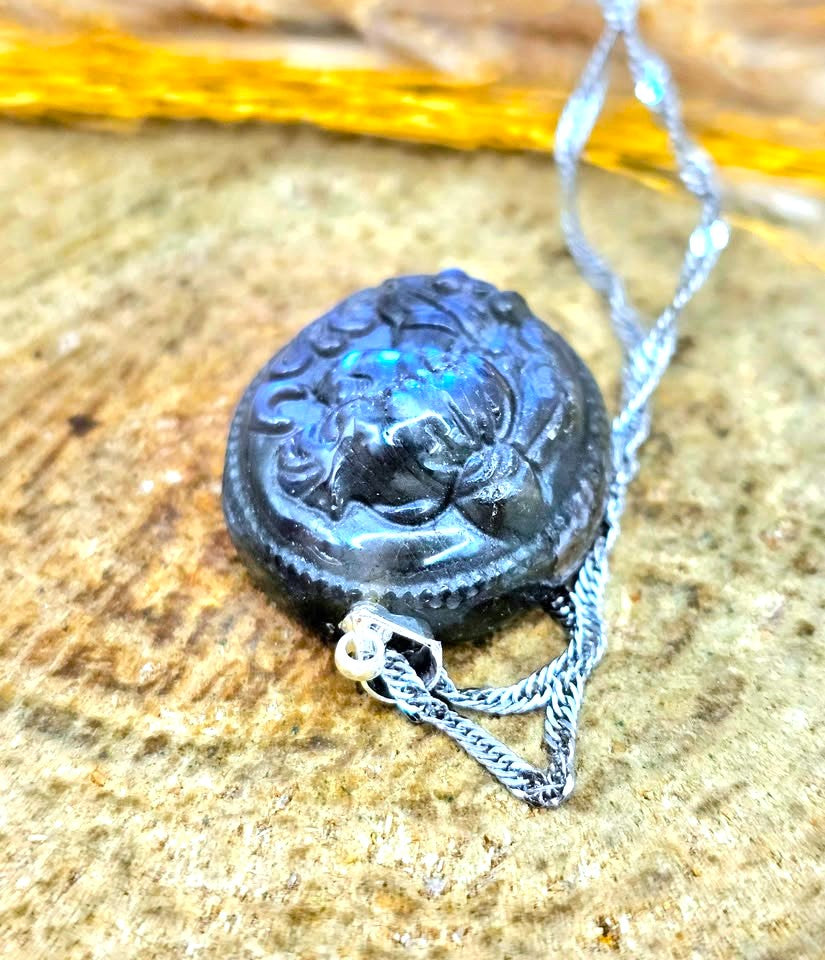 A dark carved pendant necklace with a silver-toned chain, resting on a textured stone surface.