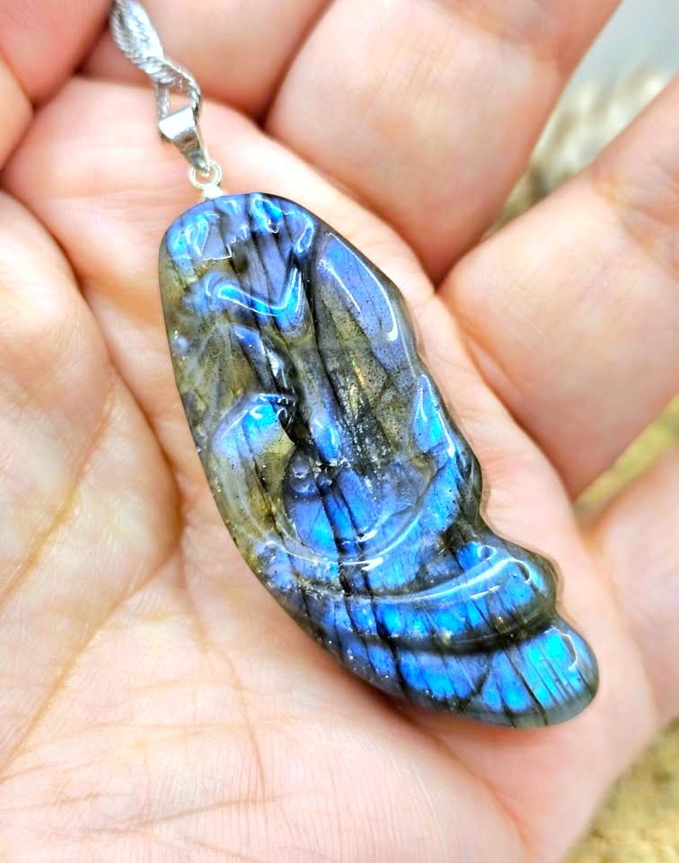 A polished labradorite pendant with vibrant blue and green iridescent flashes, held in a person's palm.