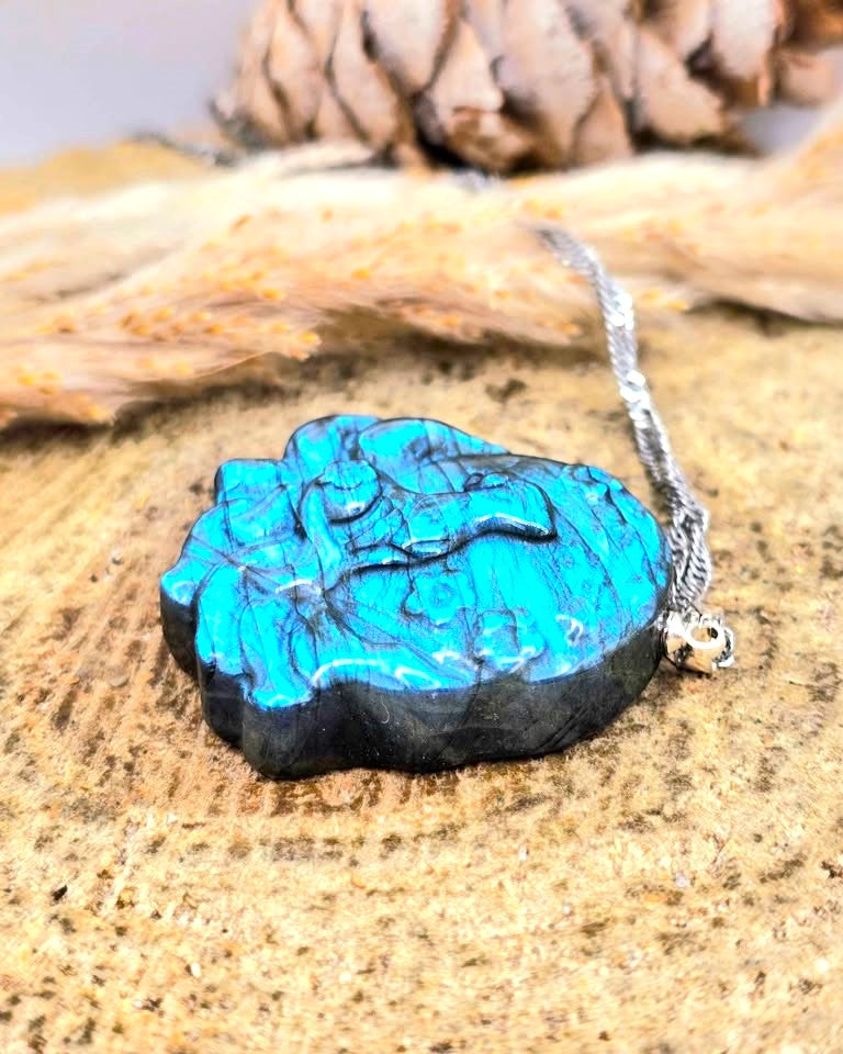 A carved wooden pendant necklace with a bright turquoise blue top layer and dark black wood underneath, hanging from a silver chain on a textured wood surface.