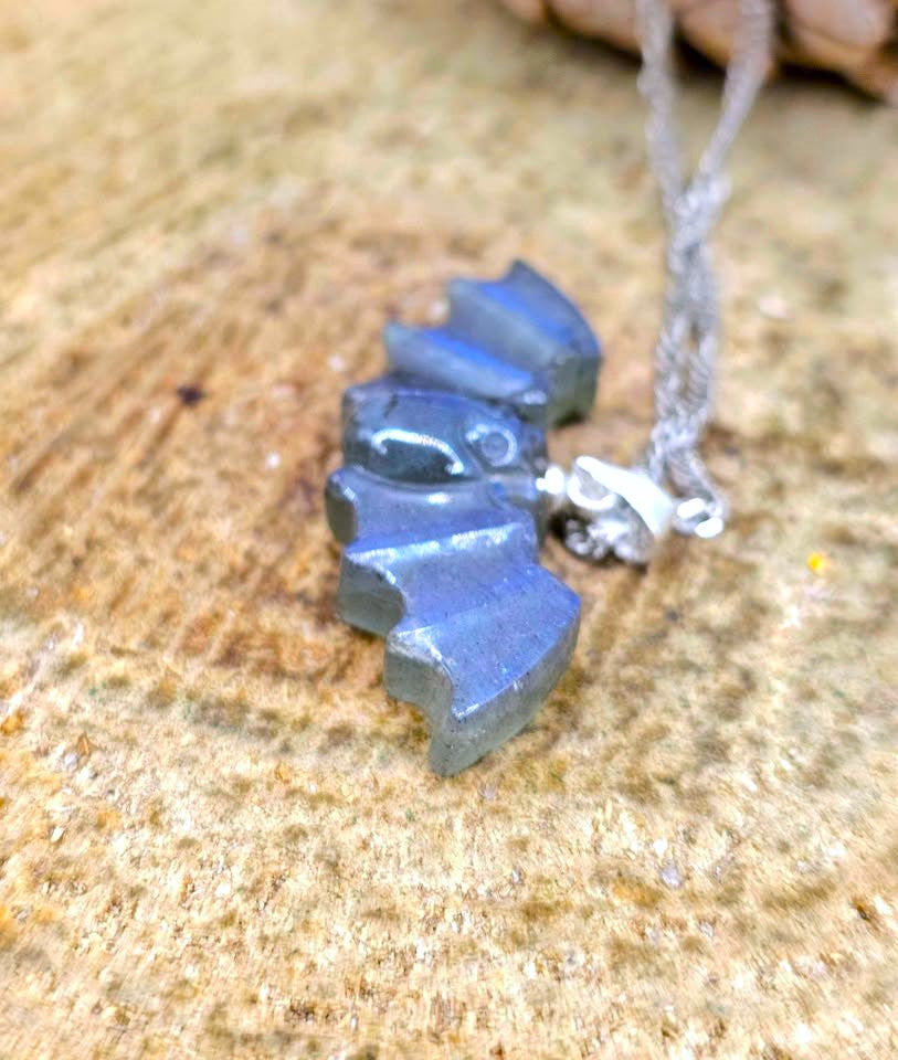 A close-up of a silver necklace with a small, irregularly shaped dark gray pendant resting on a textured tan surface.