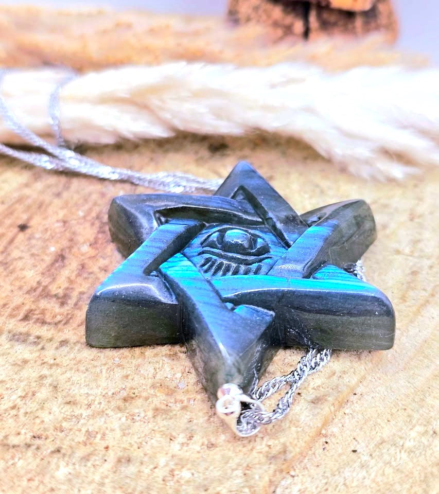 A carved black star-shaped pendant necklace with a turquoise inlay and an eye motif in the center, resting on a rustic wooden surface with a silver chain.
