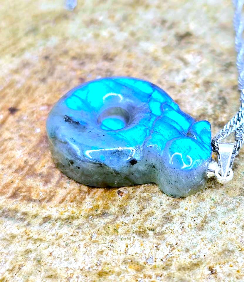 A polished turquoise and gray stone pendant necklace with a silver chain, resting on a textured sandy surface.