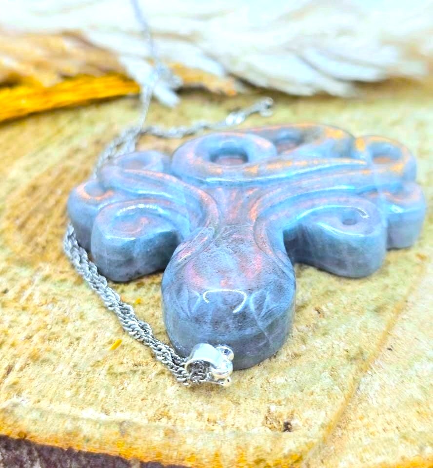 A close-up of a carved octopus-shaped pendant necklace made of blue-gray stone with subtle pinkish highlights, hanging from a silver chain on a textured wooden surface.