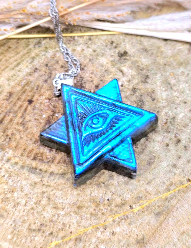 A blue and black star pendant necklace with an eye of providence design in the center, hanging from a silver chain on a textured stone surface.