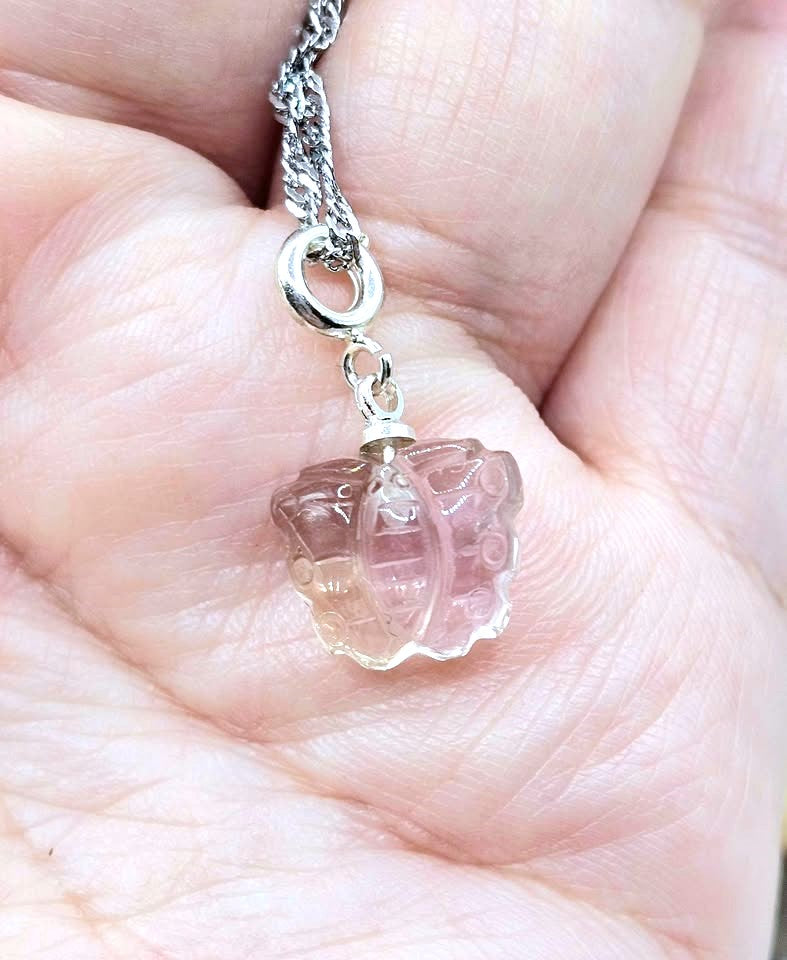 A close-up of a hand holding a silver chain necklace with a small, clear, faceted pink gemstone pendant.