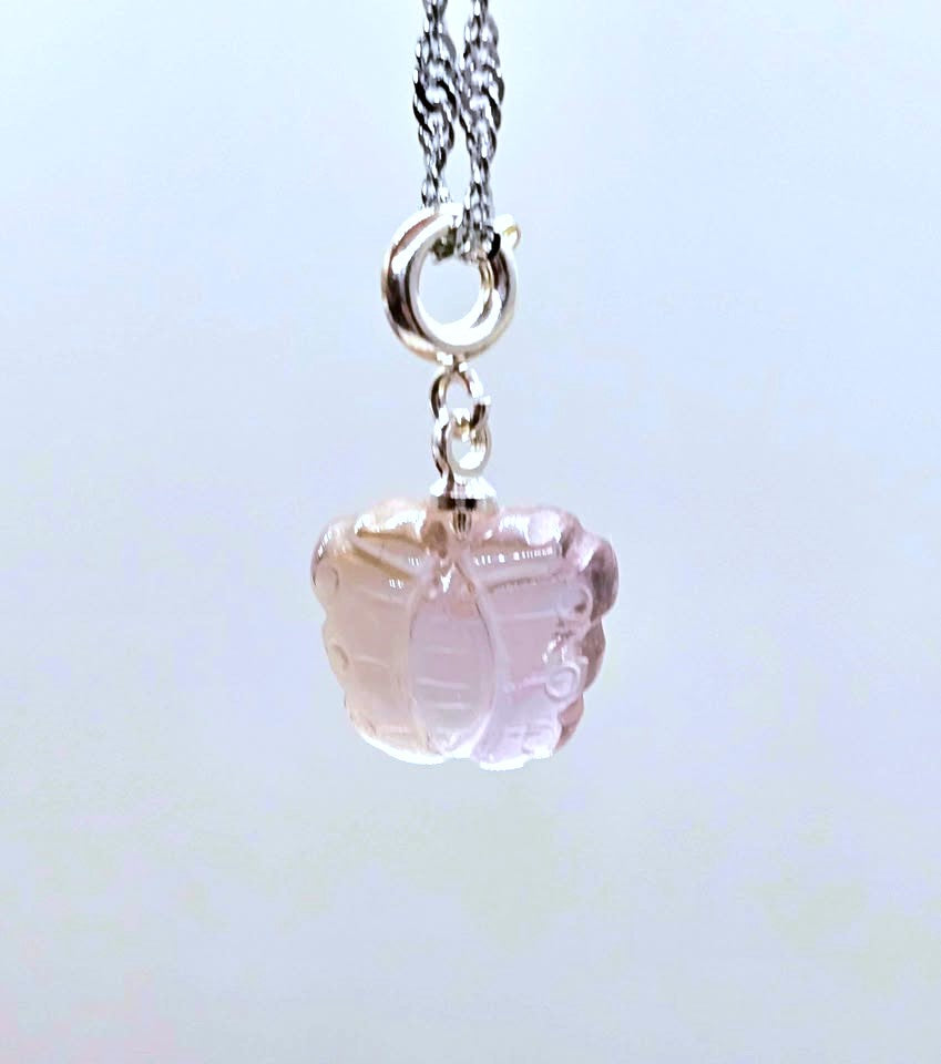 A silver chain necklace featuring a carved pale pink glass or crystal pendant, suspended against a light blue background.