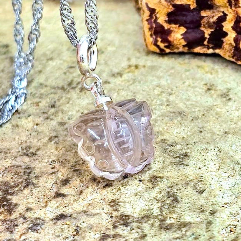 A silver chain necklace with a clear, butterfly-shaped glass or acrylic pendant, displayed on a textured stone surface with a cork piece in the background.