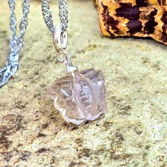 A silver chain necklace with a clear, butterfly-shaped glass or acrylic pendant, displayed on a textured stone surface with a cork piece in the background.
