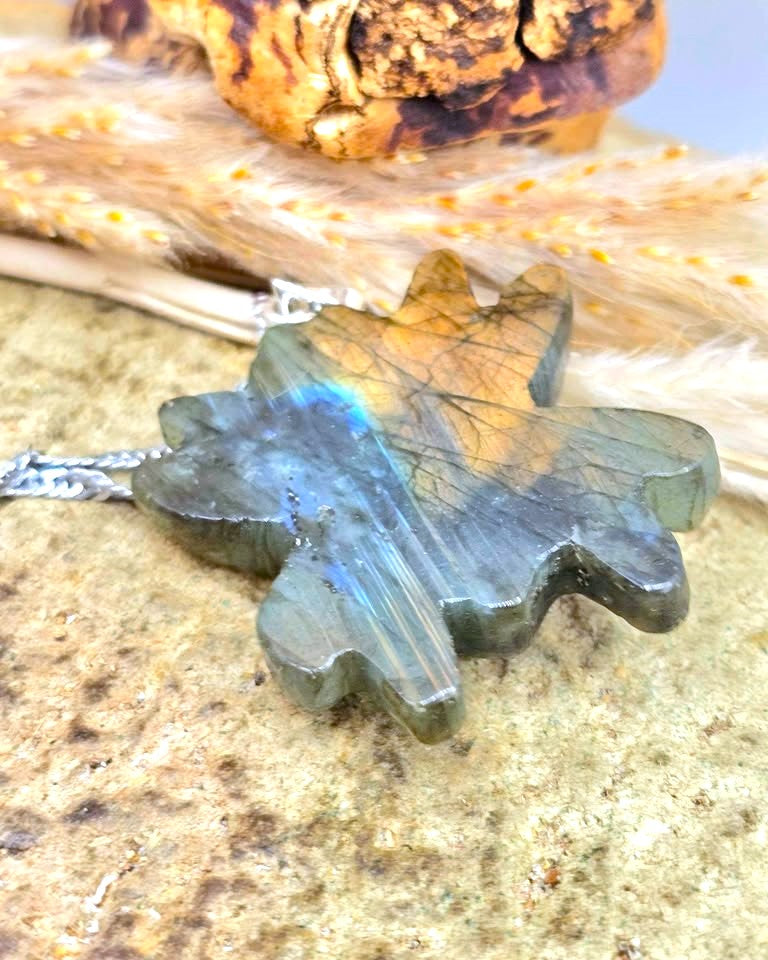 A Labradorite pendant necklace shaped like a five-pointed star, resting on a textured stone surface with dried grass and a wooden piece in the background.