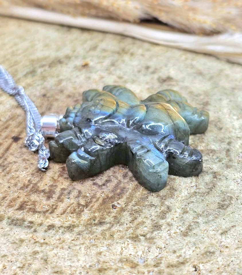 A carved Labradorite pendant with a silver bail and matching silver cord, resting on a textured stone surface.