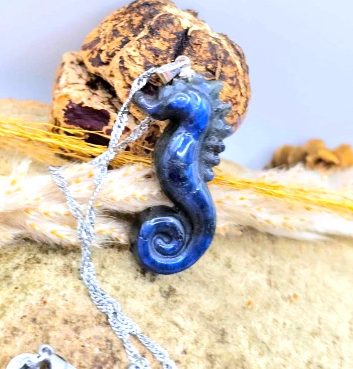 A blue seahorse pendant necklace on a silver chain, styled with a cork and natural fibers against a light background.