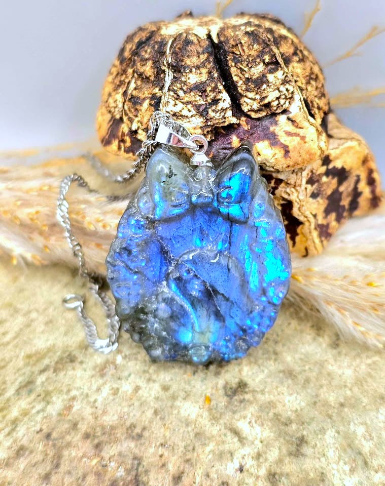 A blue labradorite totoro pendant necklace with a silver chain, displayed in front of a decorative skull and dried grass.