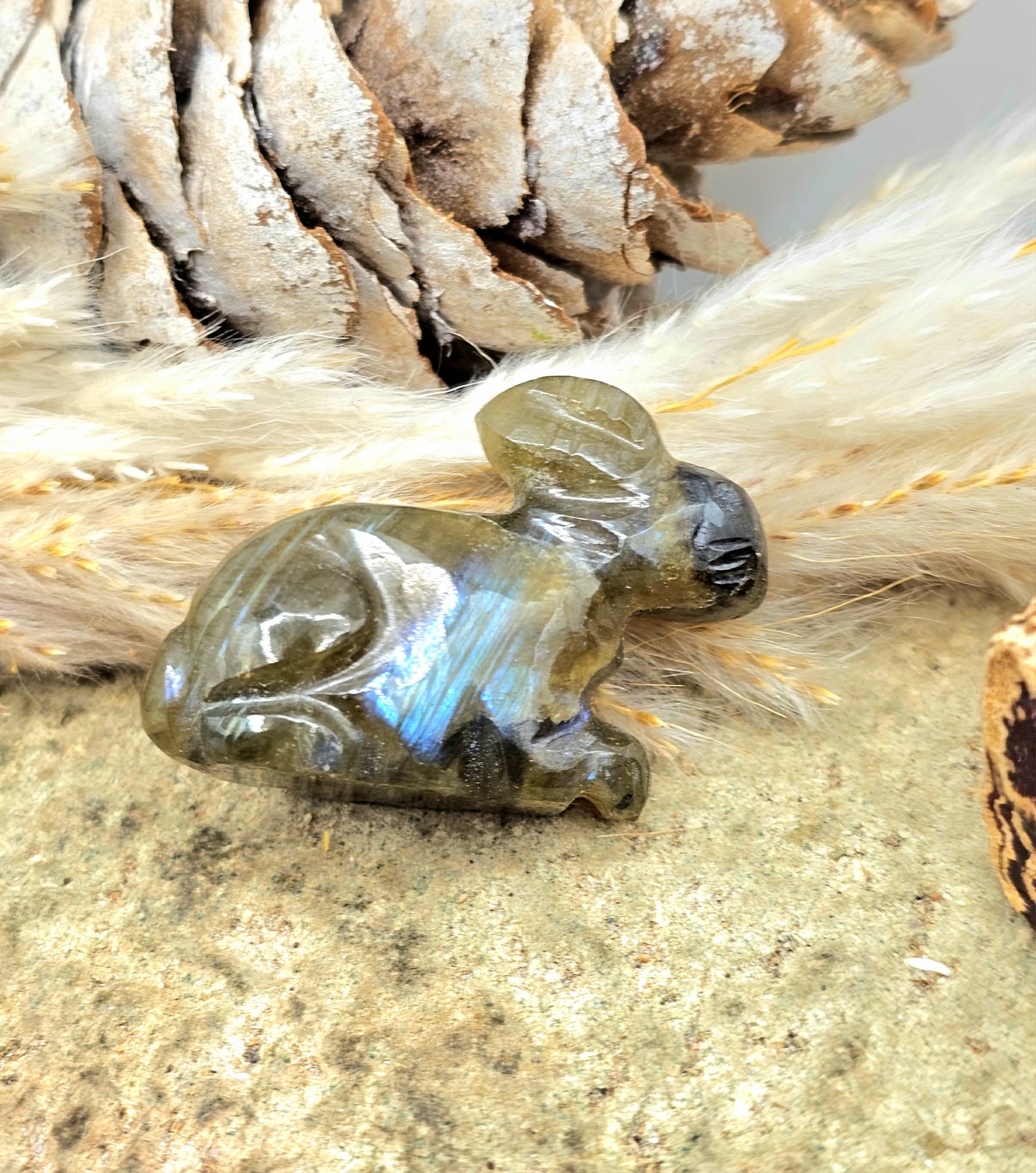 One  hand carved rabbit figurines displayed on a natural wood slice, with a pinecone and dried grass in the background.