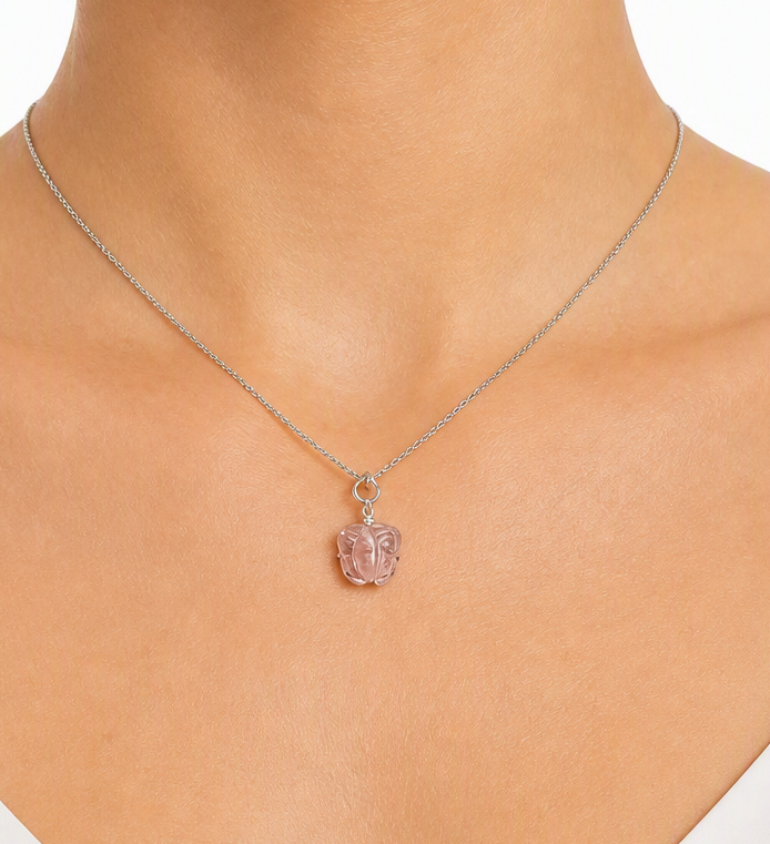 A delicate silver chain necklace with a small pink carved pendant, shown worn on a model's neck.