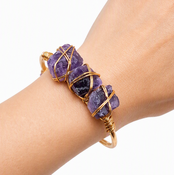A handmade cuff bracelet featuring three rough purple amethyst stones wrapped in gold-toned wire bangle wearing by human wrist-My Aura Gemstones