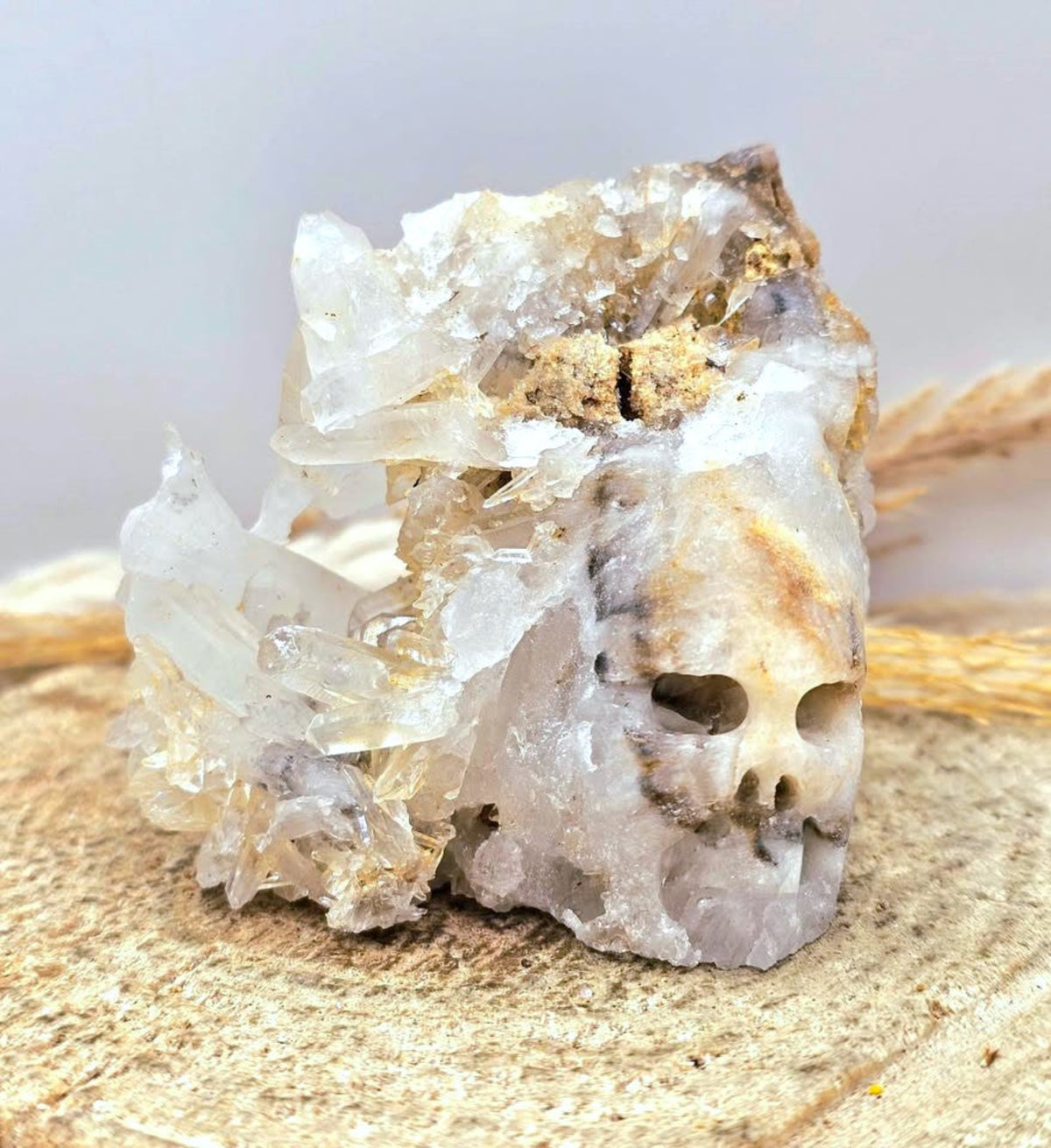 A natural crystal cluster featuring a prominent skull formation with clear quartz and beige mineral inclusions, displayed on a textured burlap surface-My Aura Gemstones. 