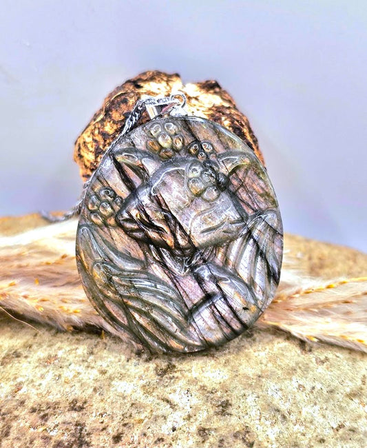 A round natural labradorite pendant necklace featuring a nine tailed fox with floral elements, resting on dried grass -My Aura Gemstones