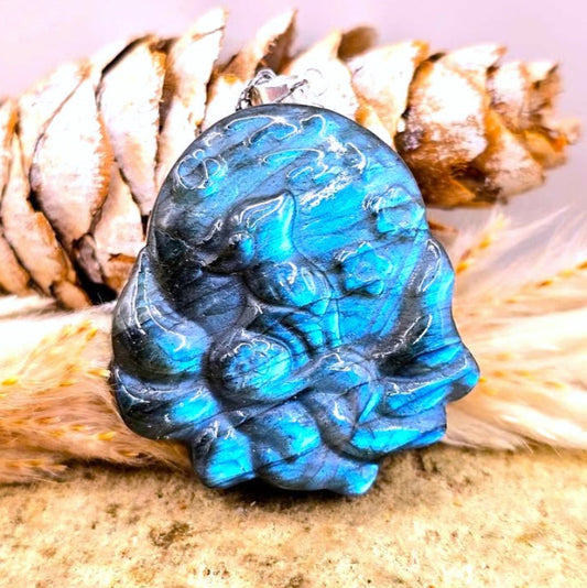 A carved blue labradorite pendant featuring a detailed nine tailed fox design, resting on a textured beige surface with a soft white faux fur accent and a silver chain.-My Aura Gemstones