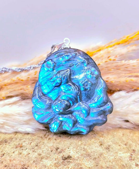 A carved blue labradorite pendant featuring a detailed nine tails fox design, resting on a textured beige surface with a soft white faux fur accent and a silver chain.-My Aura Gemstones