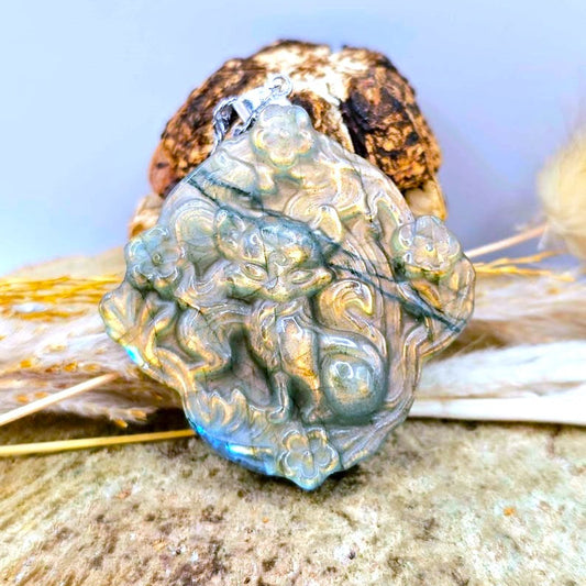 A carved blue labradorite pendant featuring a detailed nine tailed fox design, displayed on a rustic background of dried grass and wood.-My Aura Gemstones