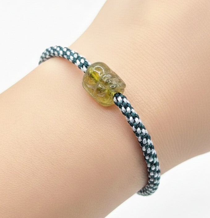 Natural Peridot carved Pi Xiu bracelet with white and dark green braided cord displayed on a white background.
