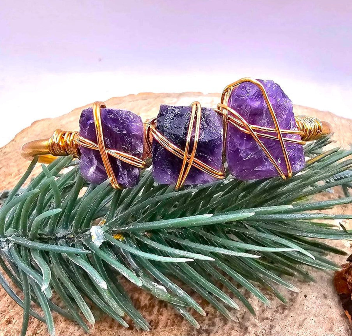 A handmade cuff bracelet featuring three rough purple amethyst stones wrapped in gold-toned wire wrapped bangle -My Aura Gemstones
